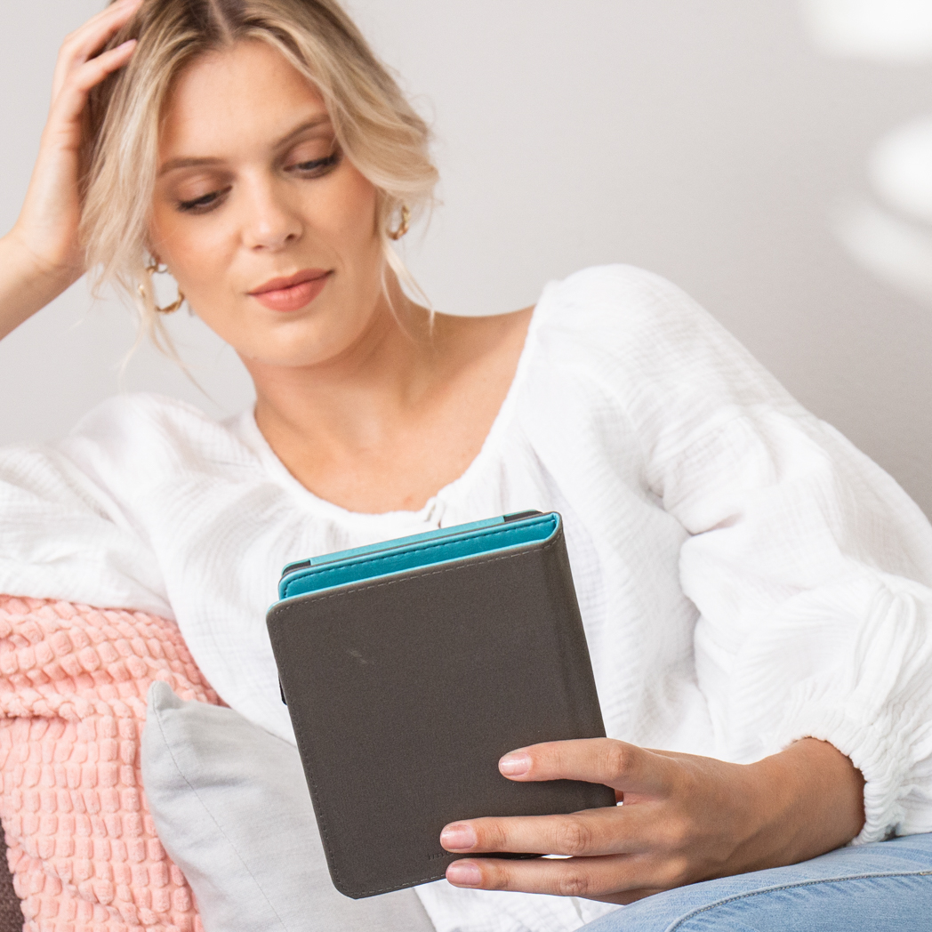 Blonde vrouw in wit shirt kijkt naar apparaat in grijsblauwe hoes.
