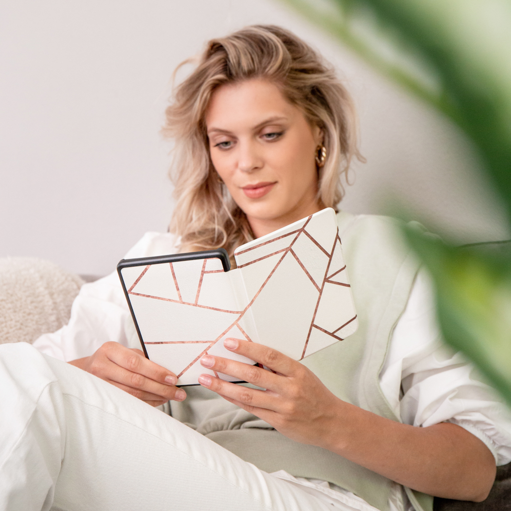 Vrouw leest e-reader met geometrische hoes. Zittend op een bank, plant op de achtergrond.