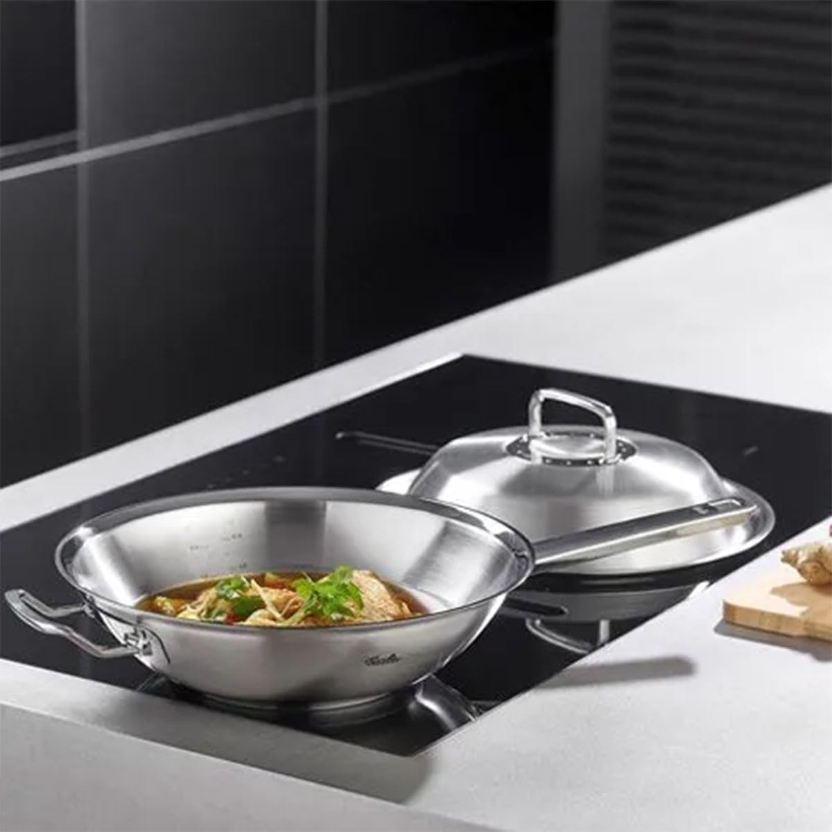 Wok in acciaio inox con cibo e coperchio su piano cottura nero. Vista dall'alto.