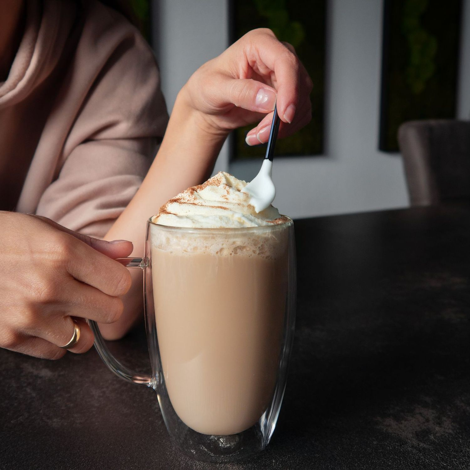 Eine Person fügt einem Kaffee in einem transparenten Glasbecher Schlagsahne hinzu.