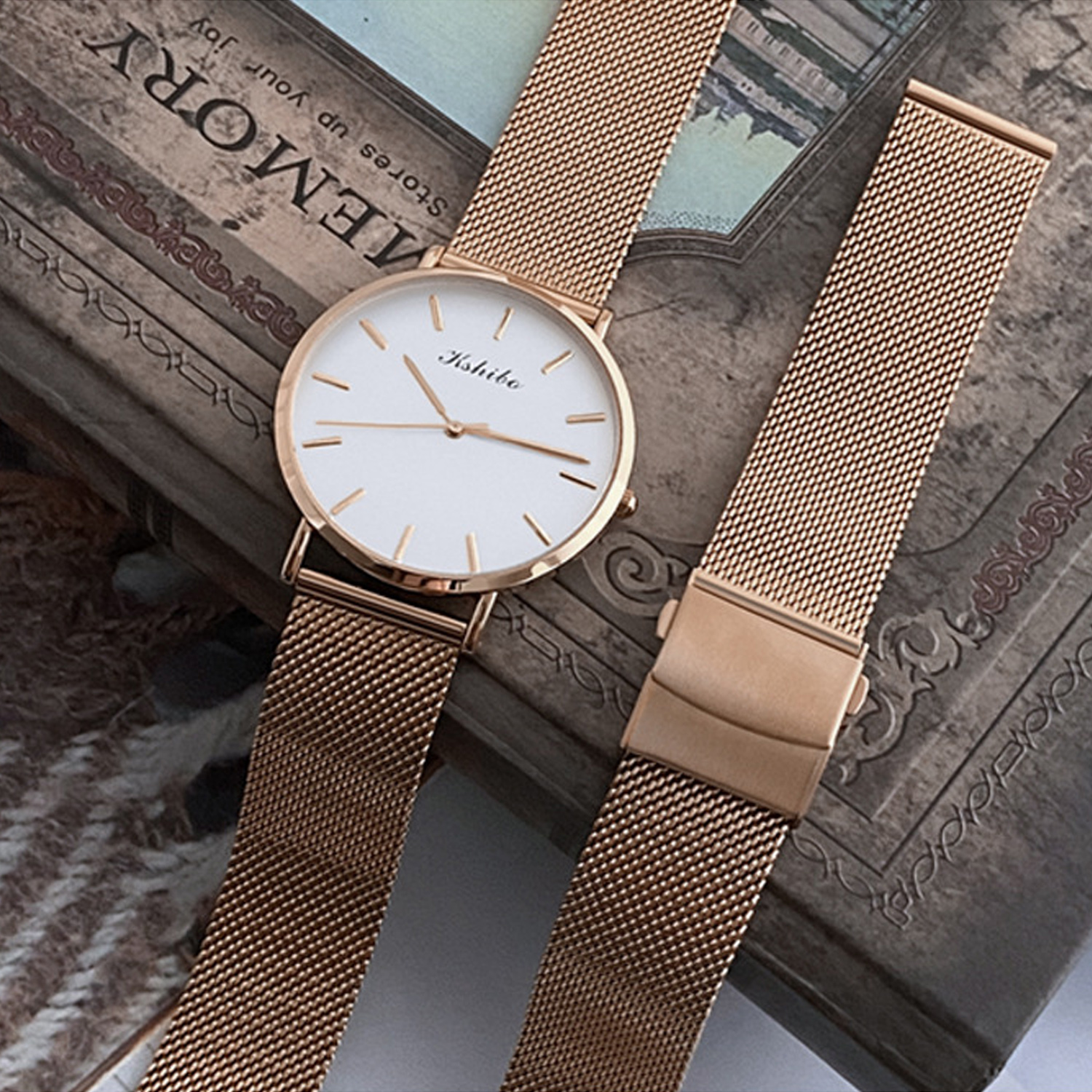 Zegarek w kolorze różowego złota z białą tarczą i bransoletą z siatki. Dodatkowy pasek obok zegarka.