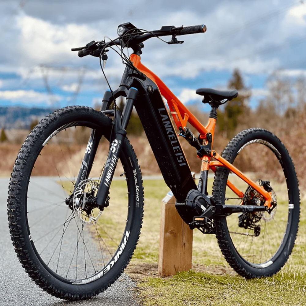 Mountain bike arancione e nera su un sentiero. Il cielo è nuvoloso. La bici ha la scritta LANKLEISI.