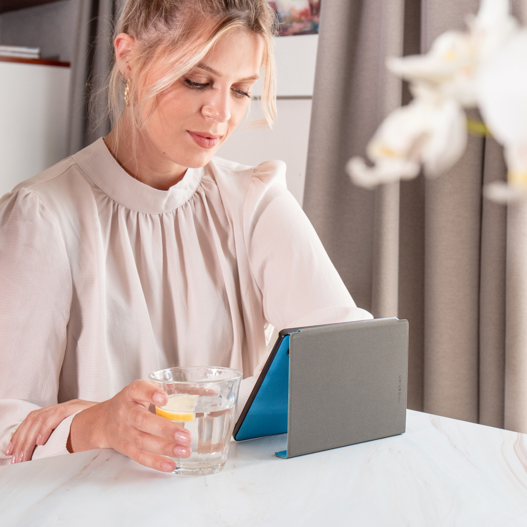 Une femme regarde une tablette. Il y a un verre d'eau avec du citron et une fleur floue.