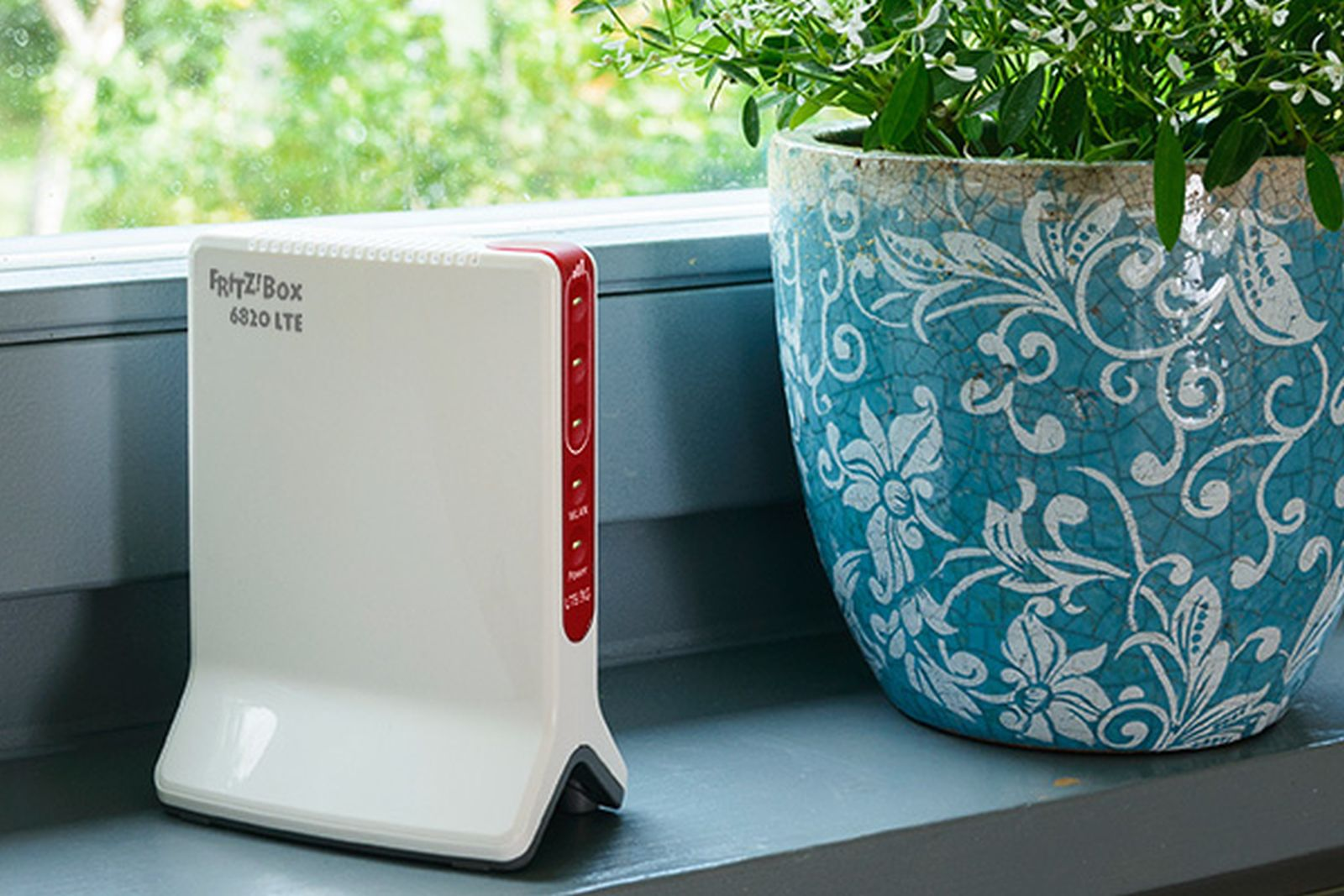 Ein weiß-roter Router auf einer Fensterbank neben einem blau-weißen Blumentopf.
