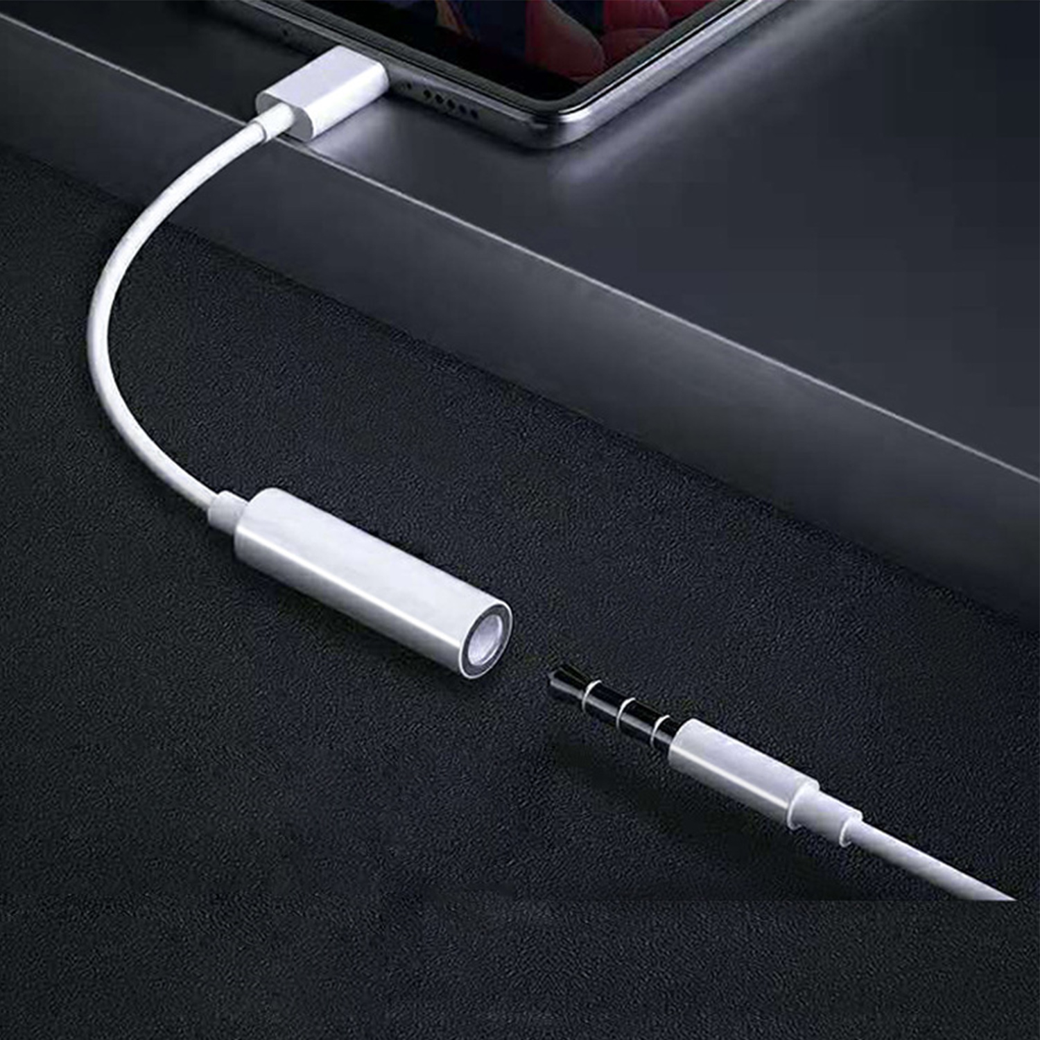 Cavo bianco con connettore collegato a un telefono e jack audio su superficie nera.