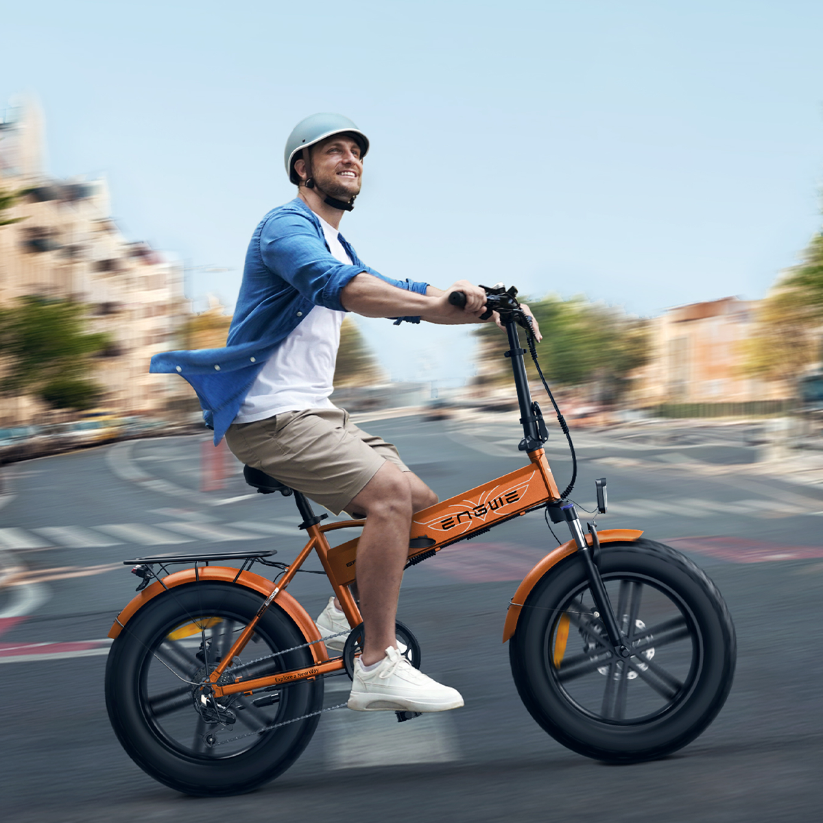 Mężczyzna jedzie pomarańczowym rowerem elektrycznym. Ma na sobie kask i uśmiechnięty patrzy w górę.