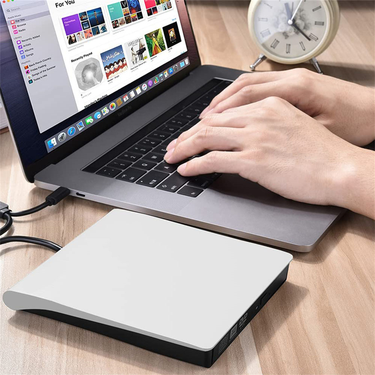 Laptop mit weißem DVD-Laufwerk. Hände tippen. Holztisch-Hintergrund.