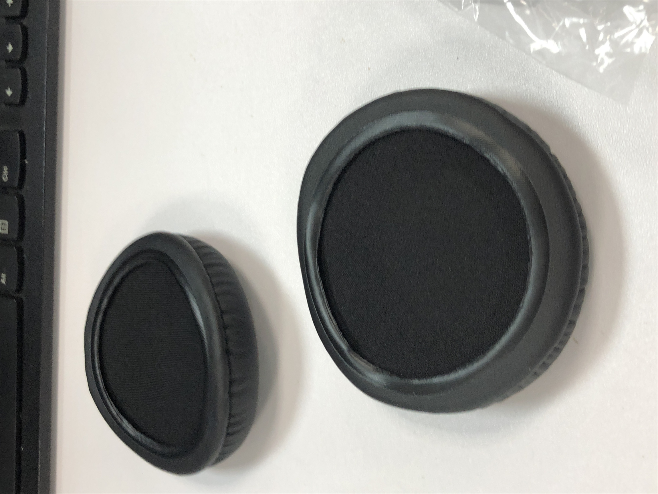 Zwei schwarze Kopfhörer-Ohrpolster mit schwarzem Stoff, weißer Hintergrund.