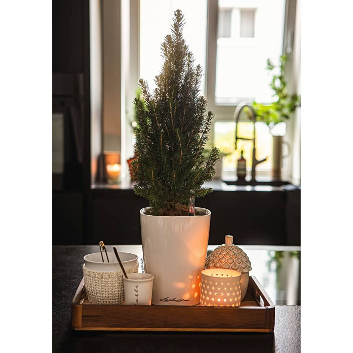 Arbre de Noël dans un pot blanc sur un plateau avec bougies et décorations.