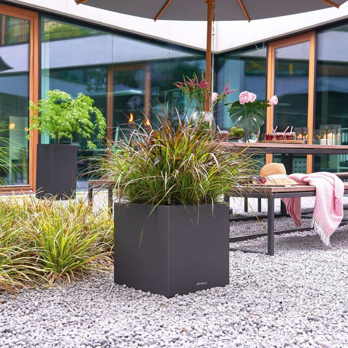 Une jardinière extérieure carrée gris foncé avec des plantes et un jardin.