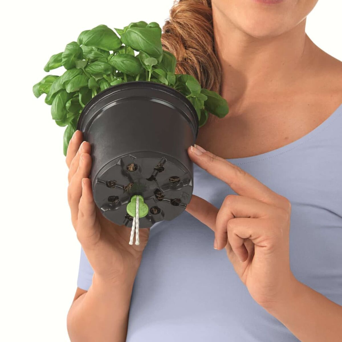 Une personne tenant un pot noir avec des plants de basilic. Le pot a une ficelle.