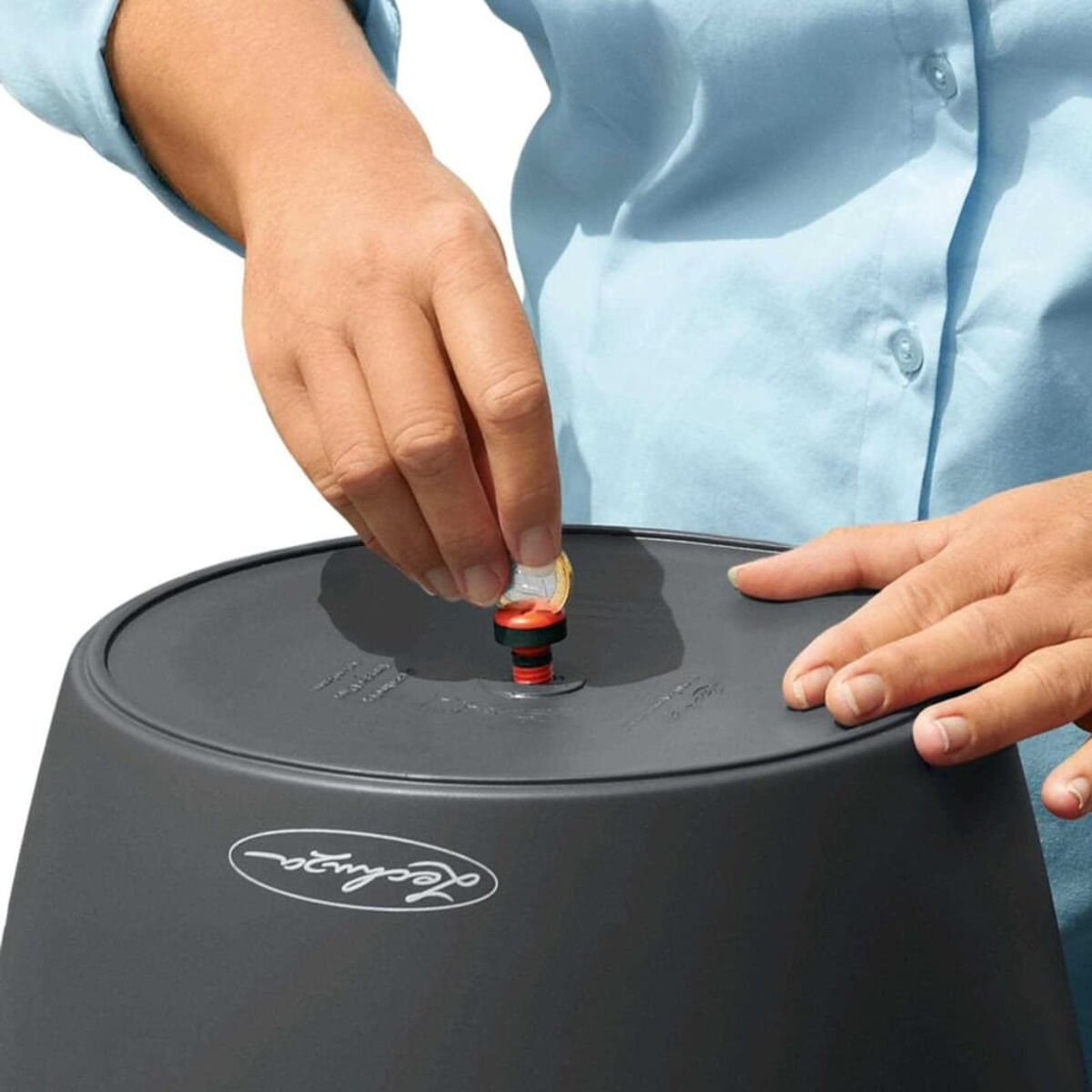 Les mains d'une personne ajoutant une pièce à un pot gris foncé avec un système d'arrosage rouge et noir.