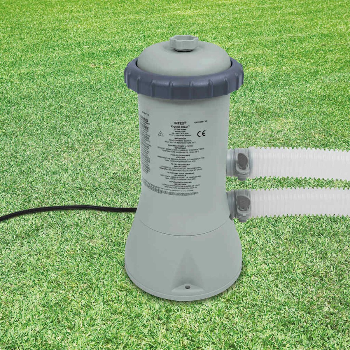 Eine graue Poolfilterpumpe auf grünem Gras. Sie hat zwei weiße Schläuche und ein schwarzes Netzkabel.