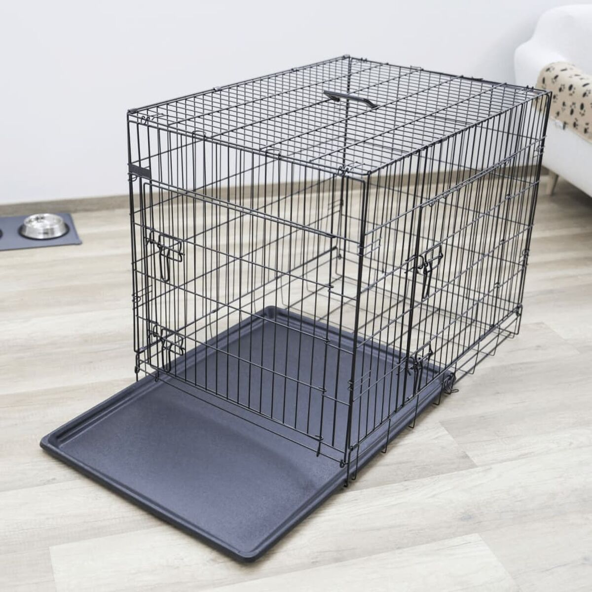 Eine schwarze Hunde-Drahtbox mit herausgezogener schwarzer Ablage. Der Hintergrund hat einen Boden und eine weiße Wand.