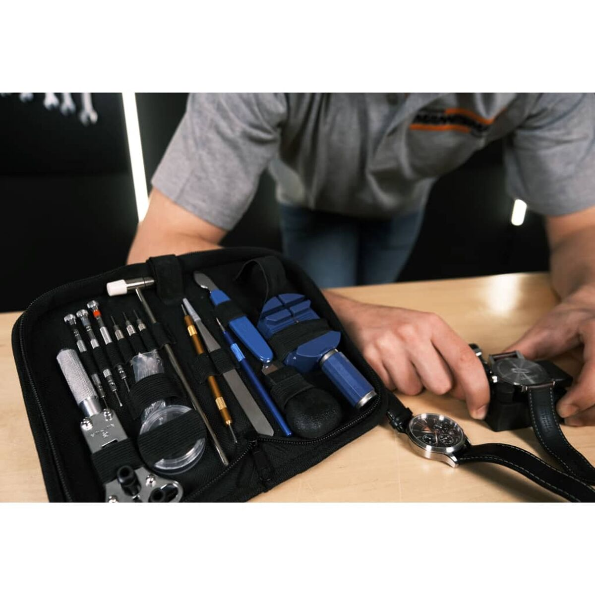 Mann arbeitet an einer Uhr mit Werkzeugen und Uhren in einem schwarzen Etui auf einem Tisch. Nahansicht.