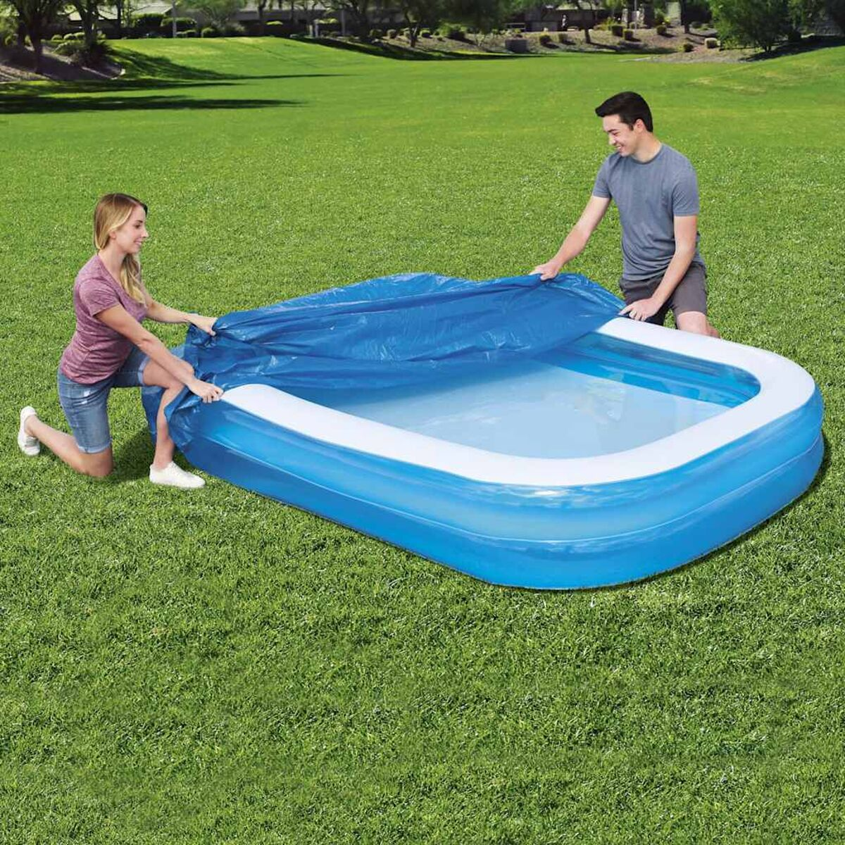 Zwei Personen bedecken einen blauen rechteckigen Pool mit einer blauen Abdeckung auf Rasen.
