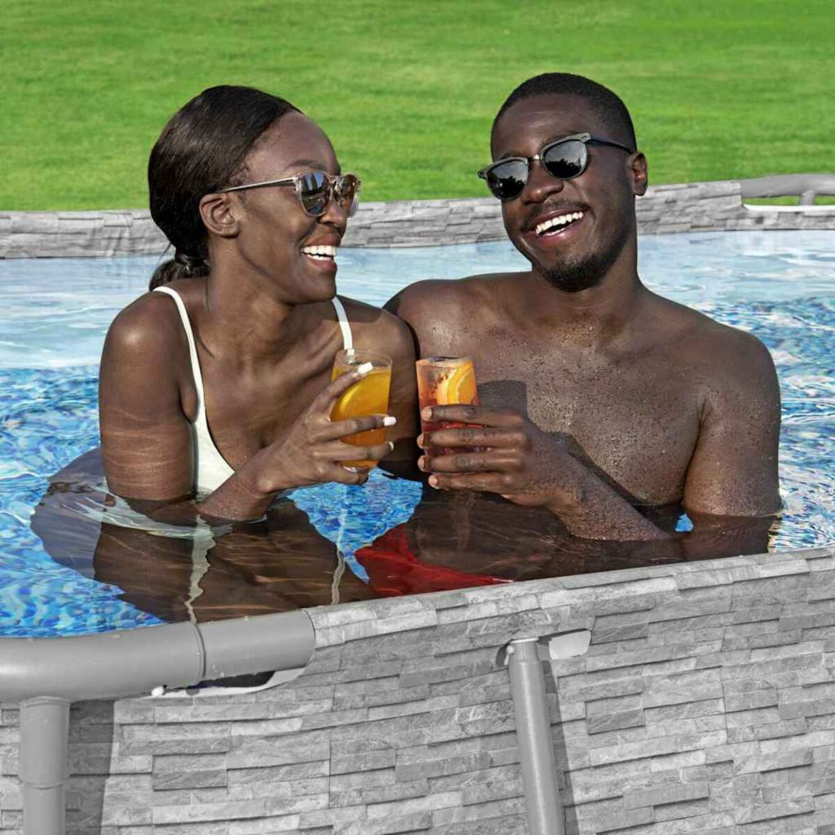 Zwei Personen im Pool, lächelnd, halten Getränke. Hintergrund: Poolrand, Gras.