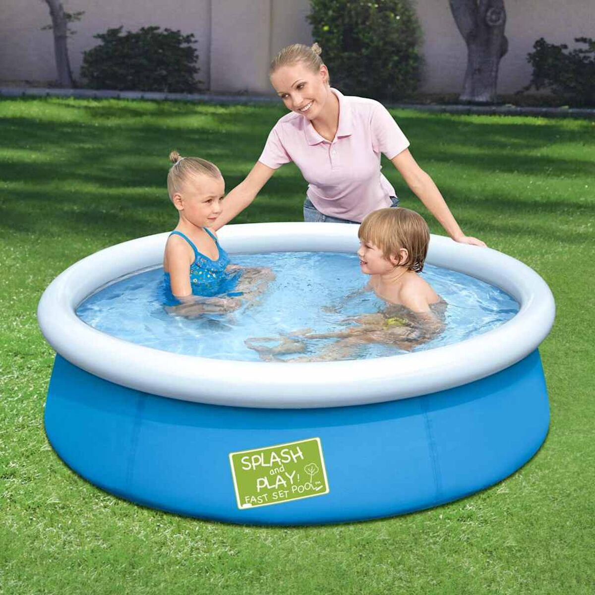 Drei Kinder und eine Frau in einem blauen aufblasbaren Pool in einem grasbewachsenen Garten.