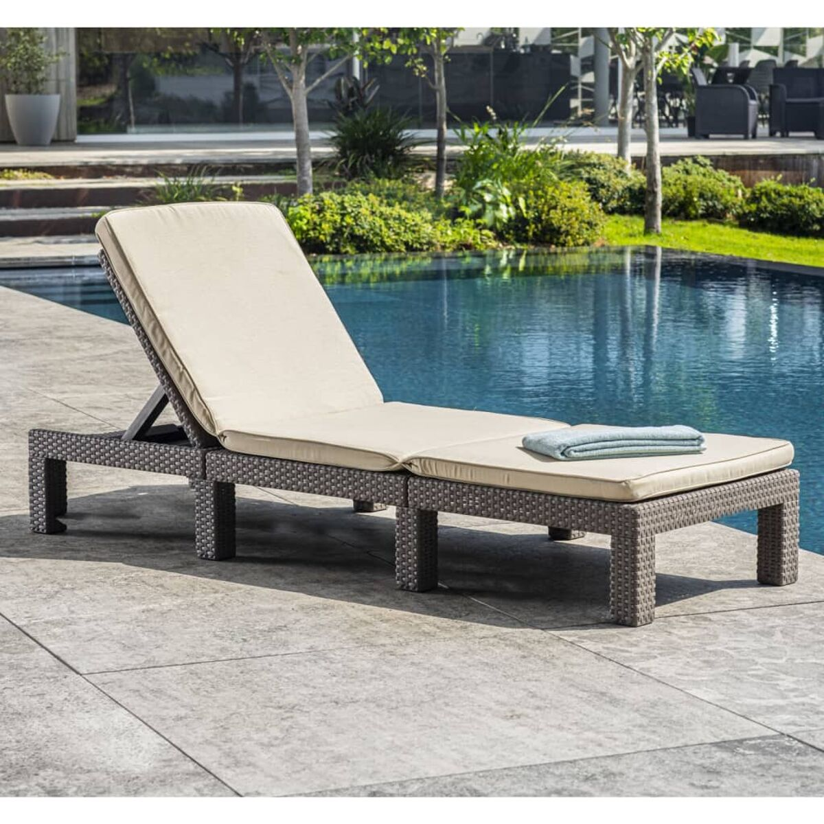 Sonnenliege aus Korbgeflecht am Pool. Ein Handtuch liegt auf der Liege.