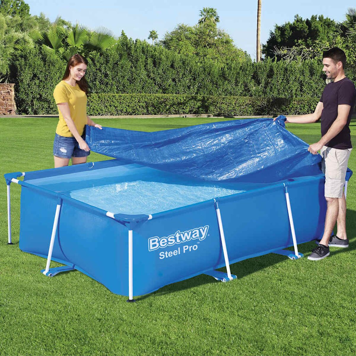 Ein Paar bedeckt einen rechteckigen blauen Pool mit einer blauen Abdeckung, auf grünem Gras.