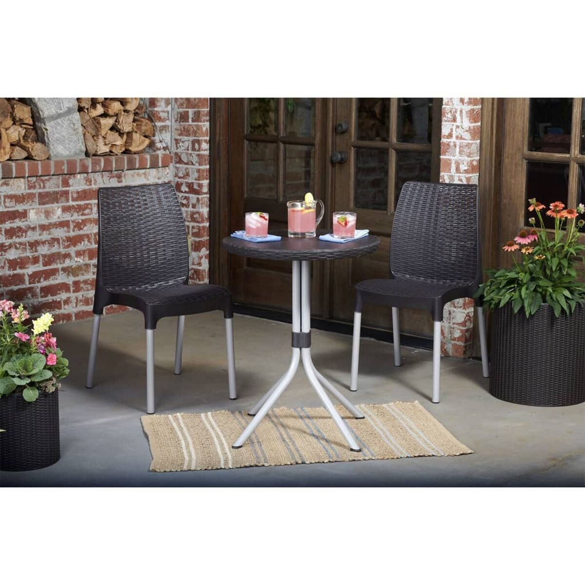 Terrassenmöbel-Set mit zwei Stühlen, einem Tisch und einem Teppich. Zwei Getränke auf dem Tisch. Blumen in Töpfen.