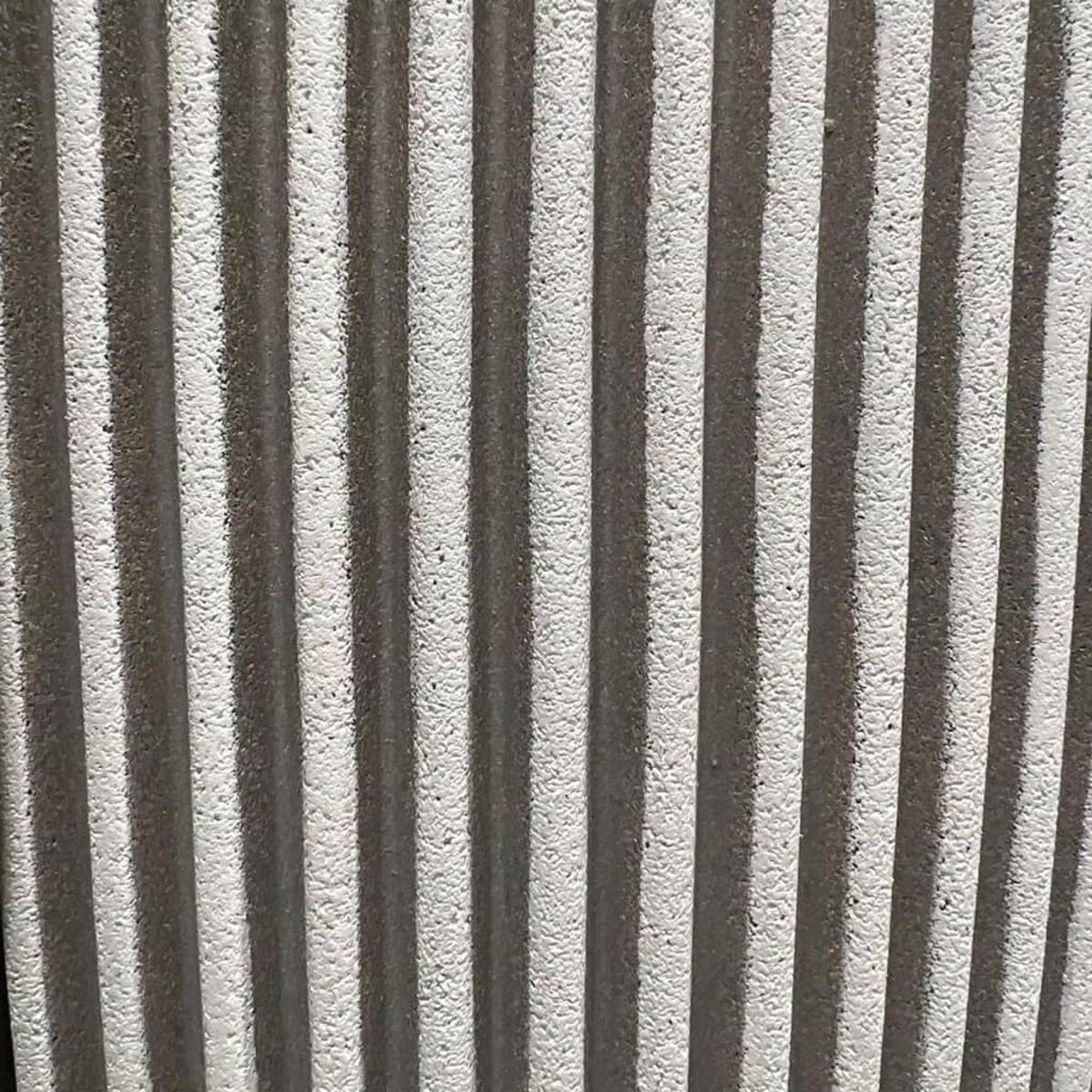 Nahaufnahme einer strukturierten Wand. Vertikale, hellgraue Linien mit Schatten dazwischen.