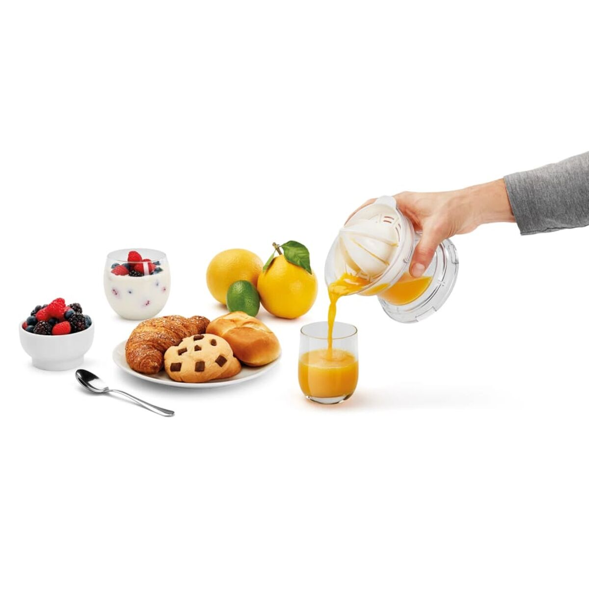 Escena de desayuno: jugo vertiéndose, frutas, pasteles, yogur con bayas y cuchara.