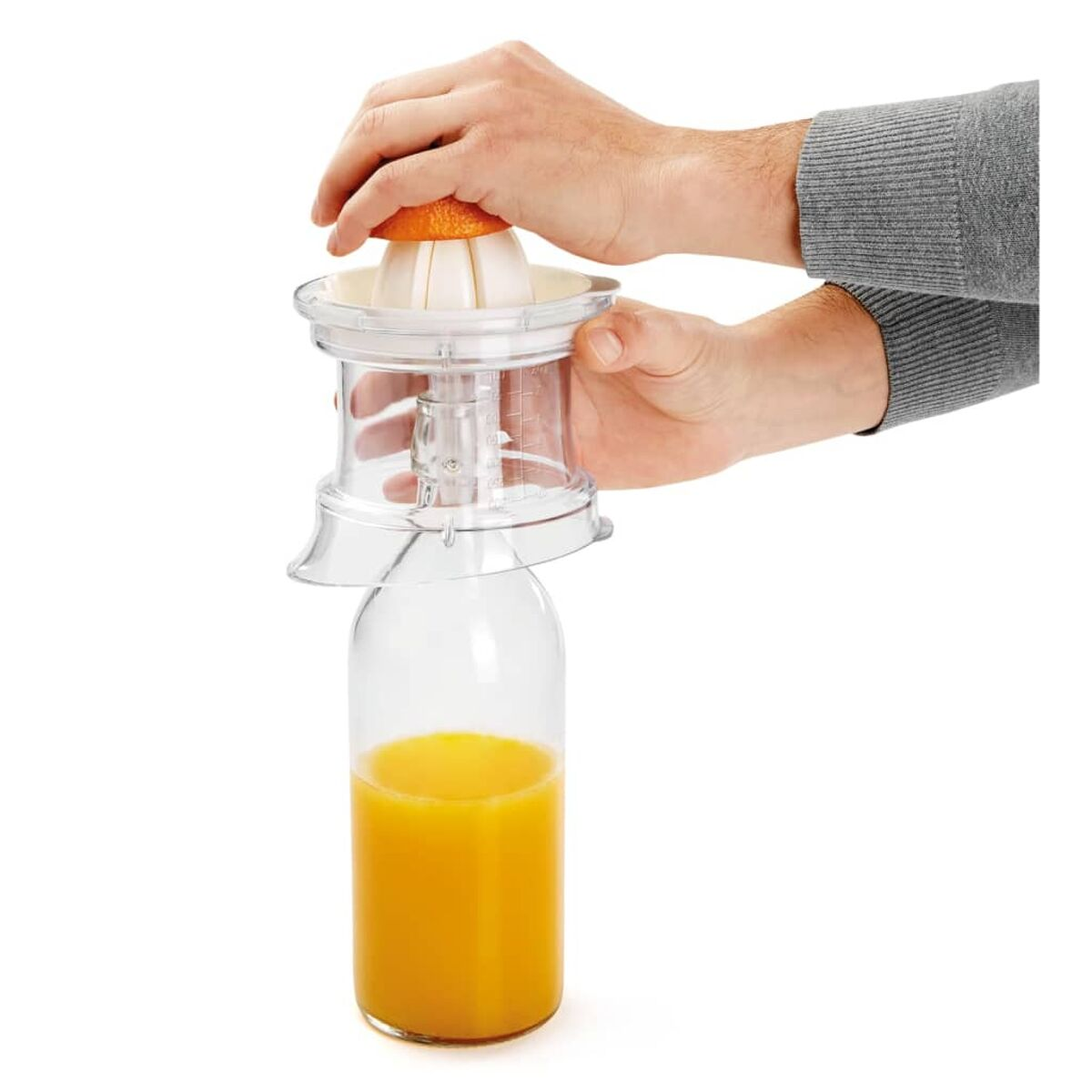 Manos exprimiendo media naranja en un exprimidor sobre una botella de vidrio con zumo de naranja.