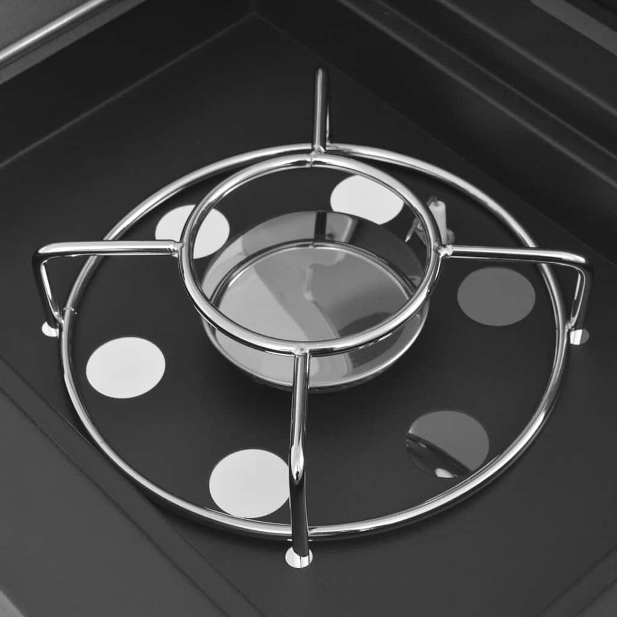 Kreisförmiger Metallgrill auf schwarzer Oberfläche mit weißen und grauen Punkten. Draufsicht.