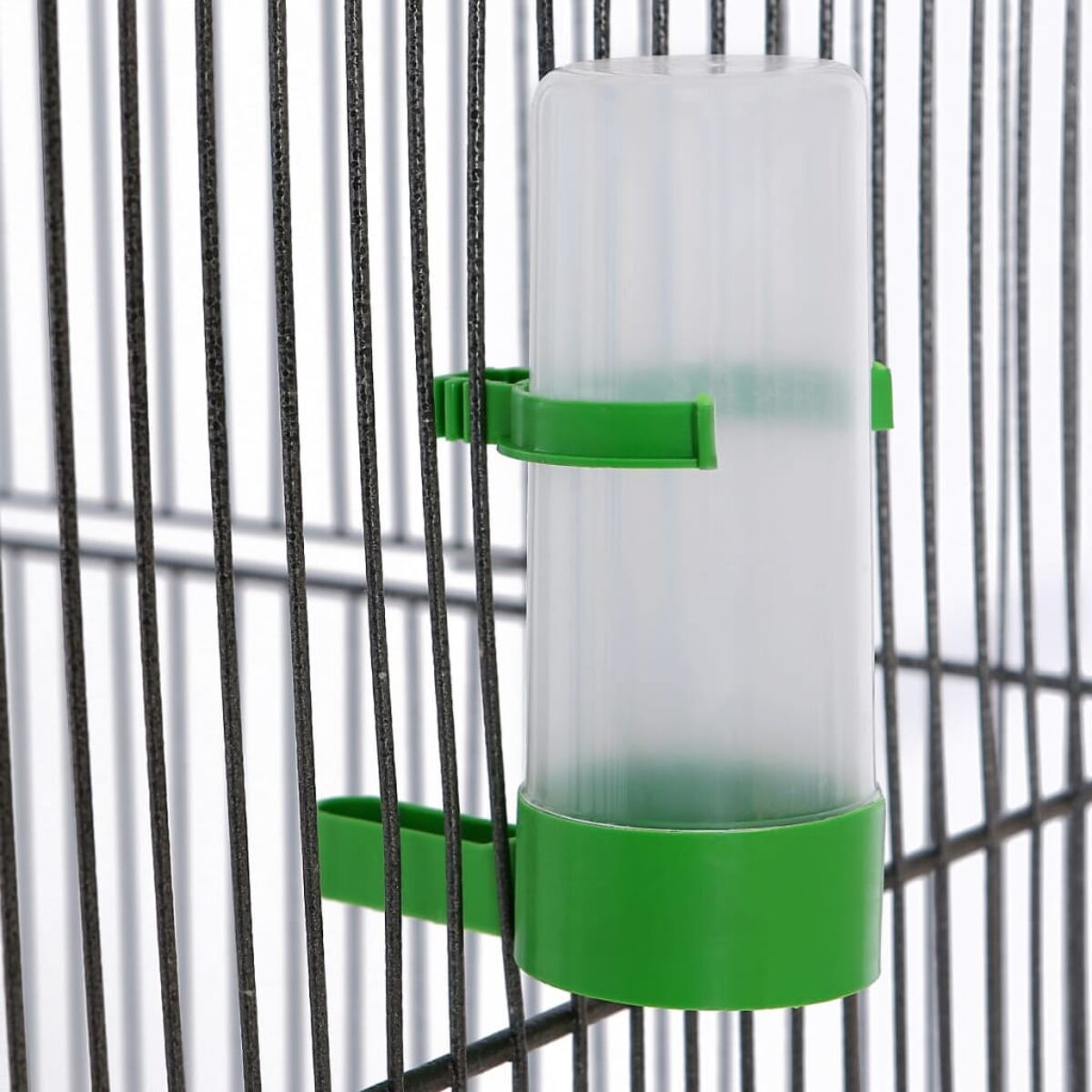 Ein grüner und weißer Vogelwasserspender an einem schwarzen Käfig befestigt.