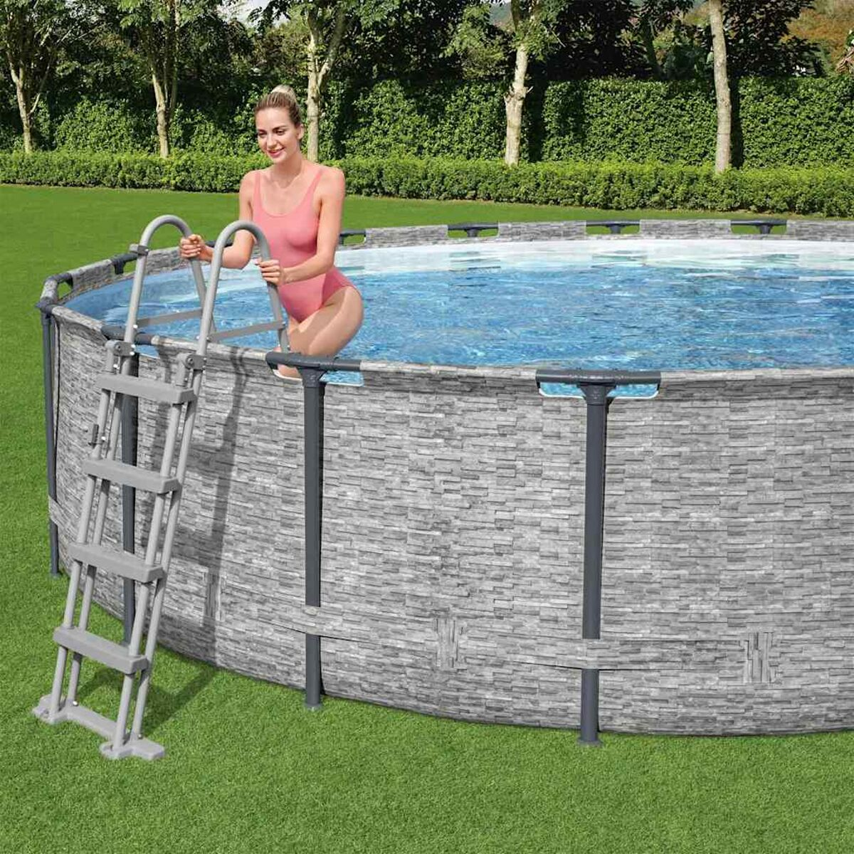 Eine Frau steigt aus einem Pool. Grau gefliester Pool und grünes Gras.