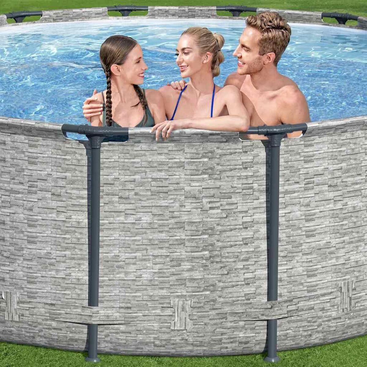 Drei Personen lächeln in einem Schwimmbecken mit einer Steinmauer.