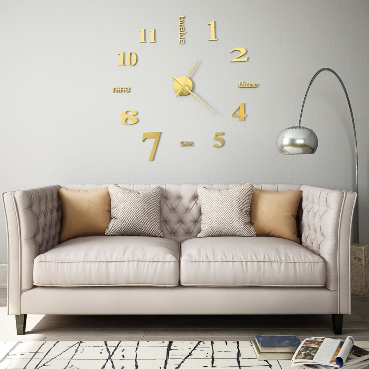 Große goldene Uhr an einer grauen Wand. Davor steht ein Sofa mit Kissen.
