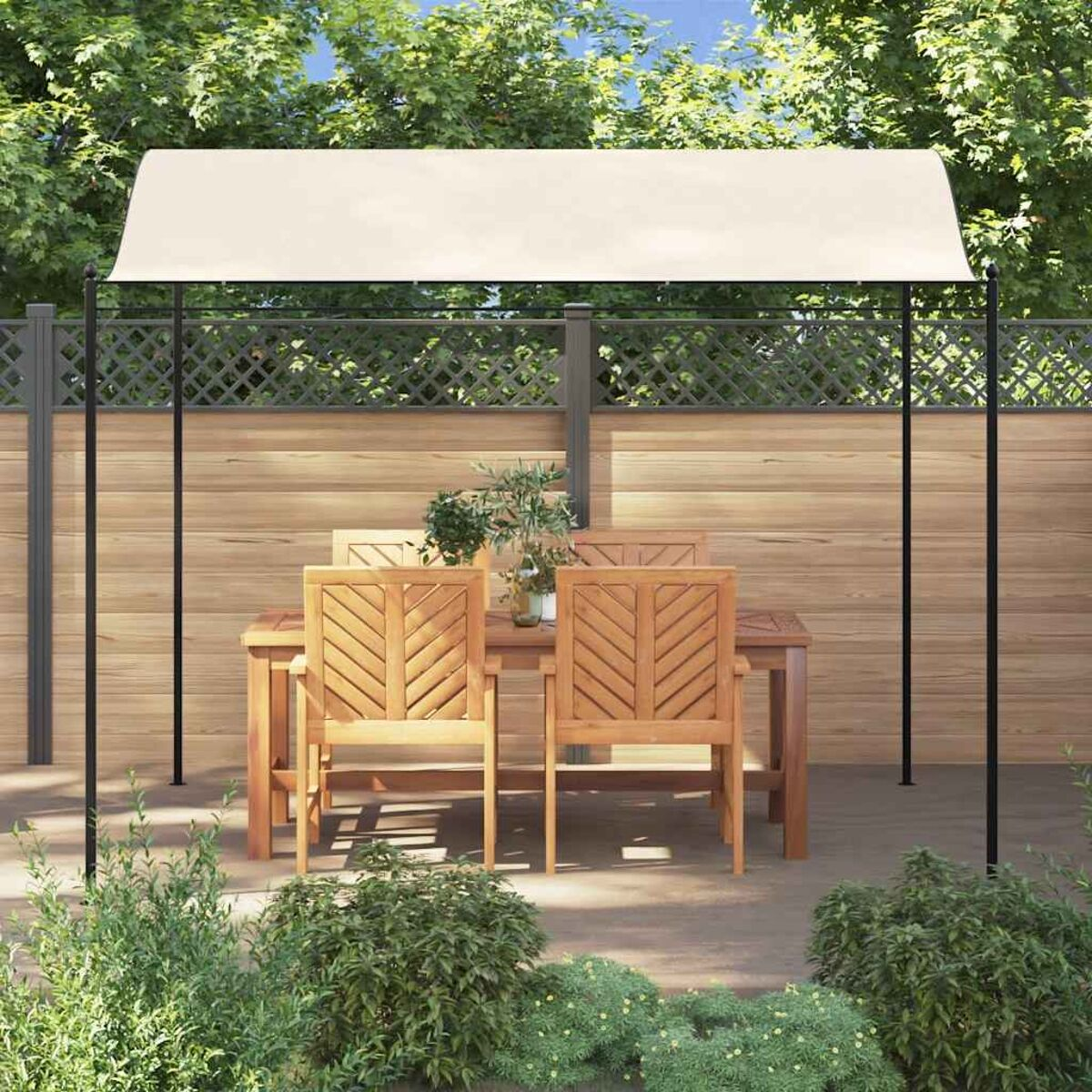 Holztisch und Stühle unter einem beigen Vordach, auf einer Terrasse mit Pflanzen und Zaun.