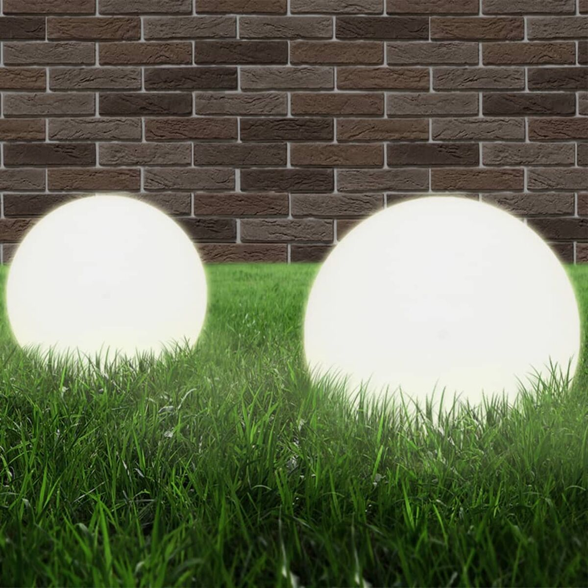Due globi bianchi luminosi nell'erba, su uno sfondo di muro di mattoni.