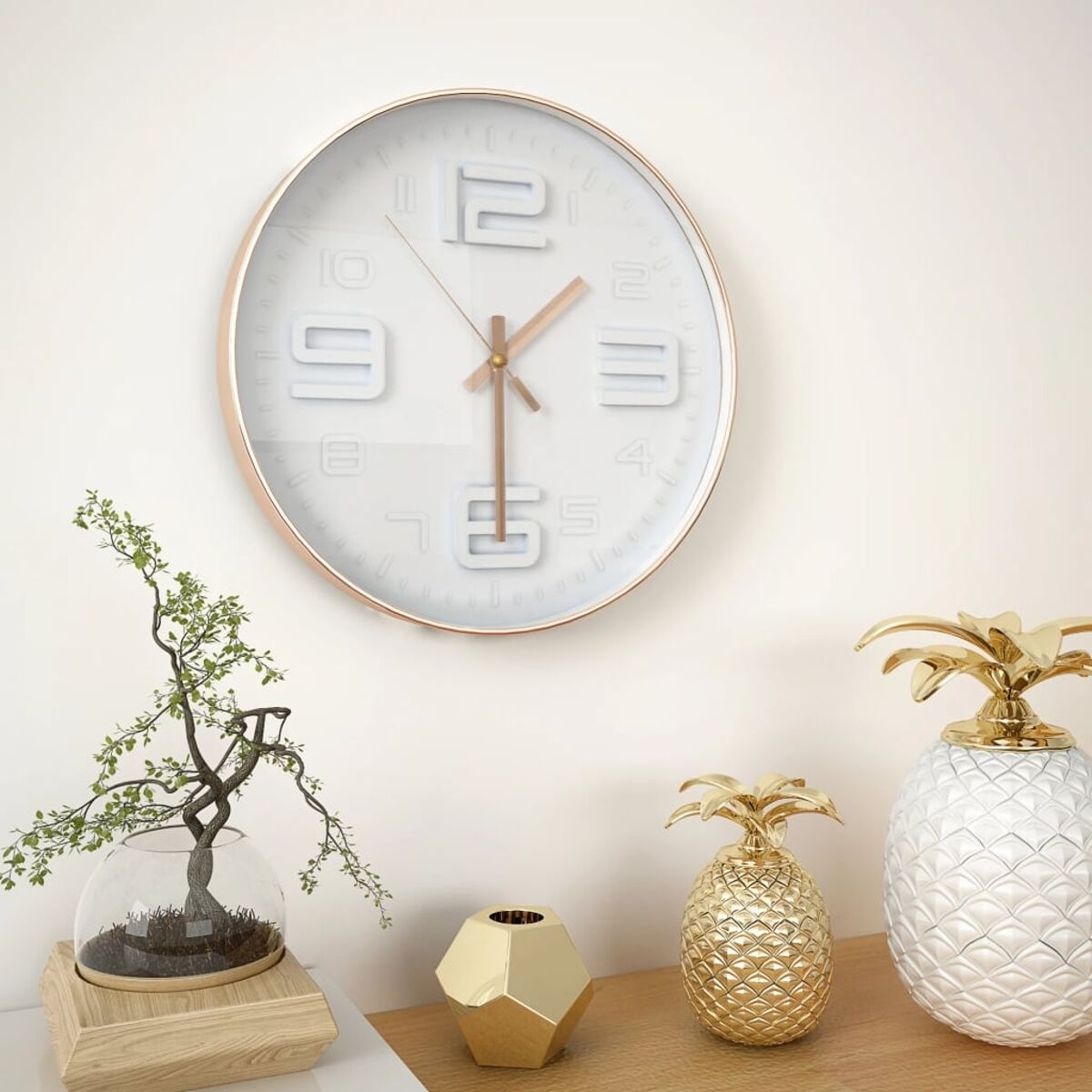 Orologio da parete rotondo bianco con bordo oro rosa. Oggetti decorativi su muro bianco.