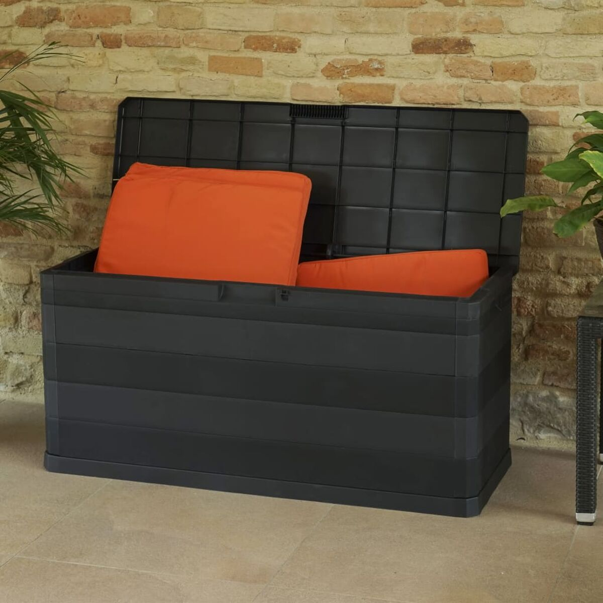 Schwarze Outdoor-Aufbewahrungsbox mit orangefarbenen Kissen, vor einer Ziegelmauer.