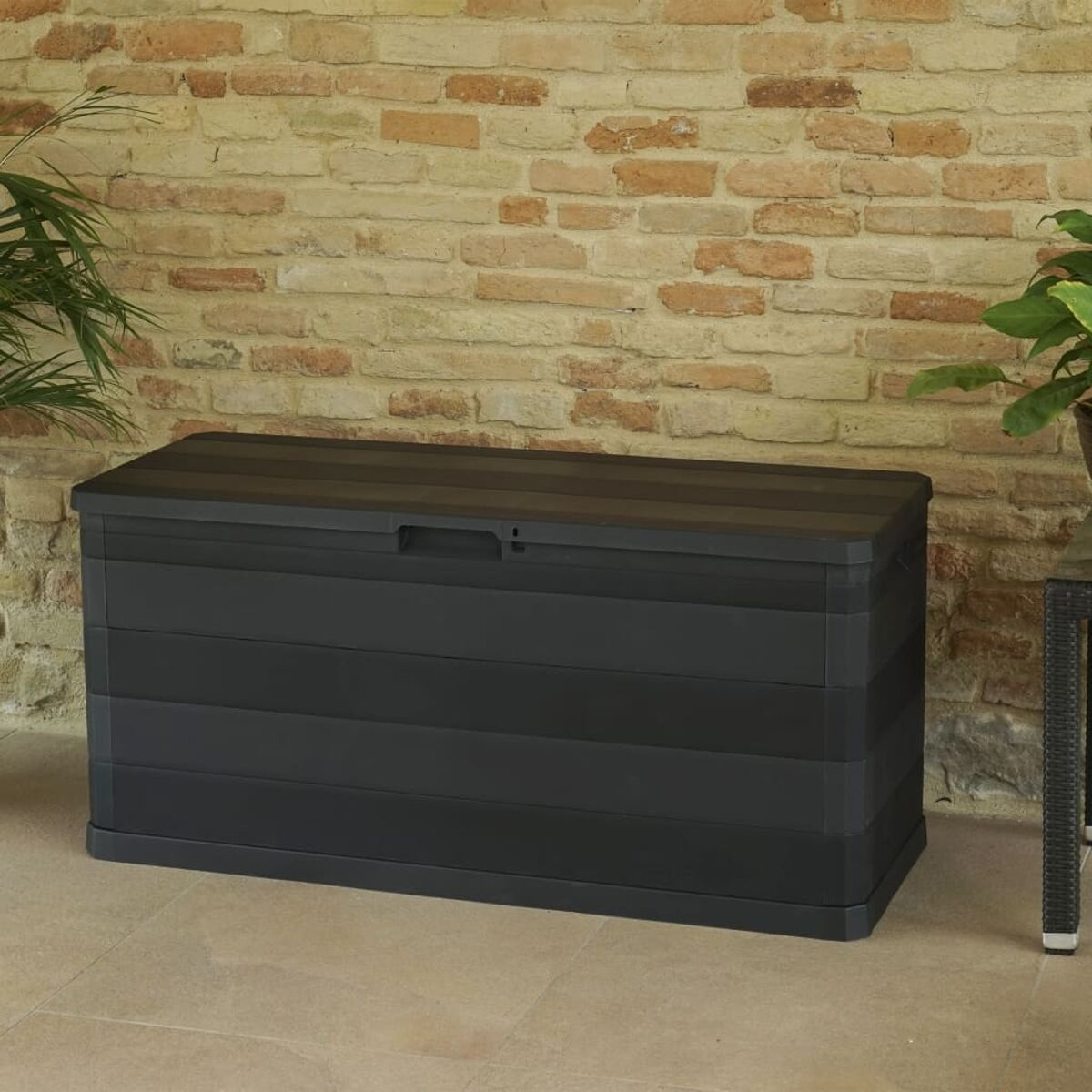 Dunkelgraue Outdoor-Aufbewahrungsbox aus Kunststoff. Ziegelmauer im Hintergrund.