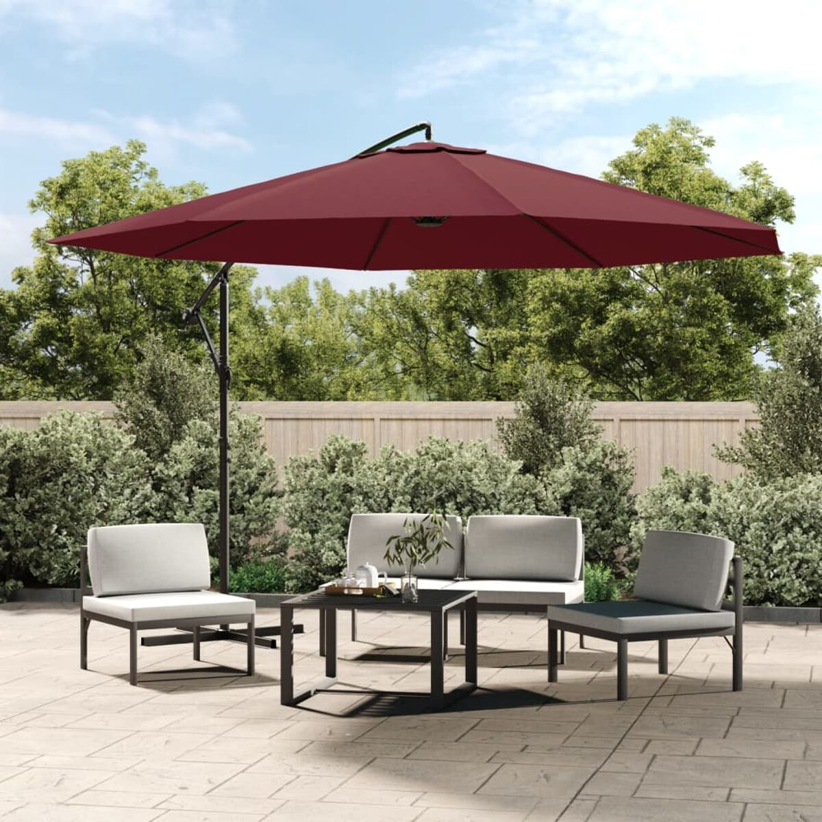 Outdoor-Sitzarrangement mit einem bordeauxfarbenen Schirm. Inklusive Stühlen, Sofa und kleinem Tisch. Grüne Bäume im Hintergrund.