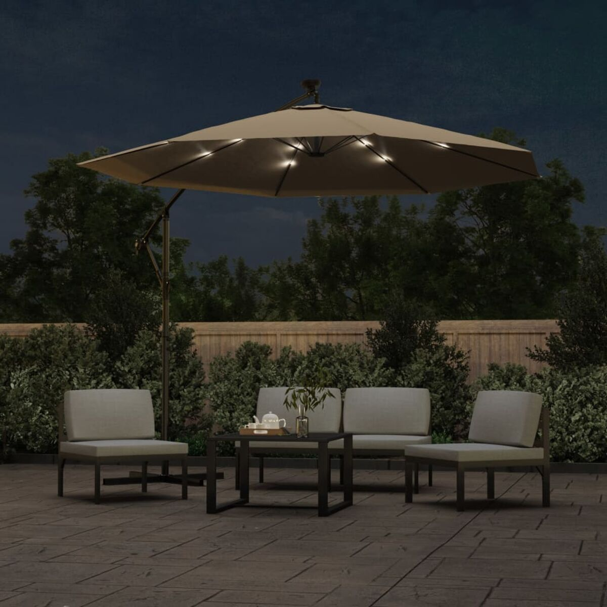 Terrassenmöbel-Set im Freien bei Nacht. Enthält einen beigen Schirm mit Lichtern, Stühle und einen Tisch.
