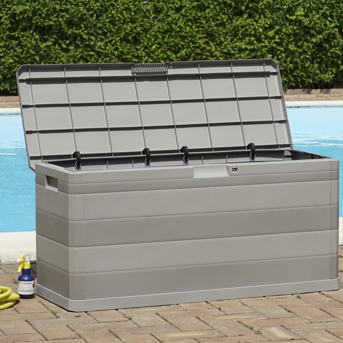 Eine graue Aufbewahrungsbox mit offenem Deckel, in der Nähe eines blauen Pools und eines gelben Gartenschlauchs.