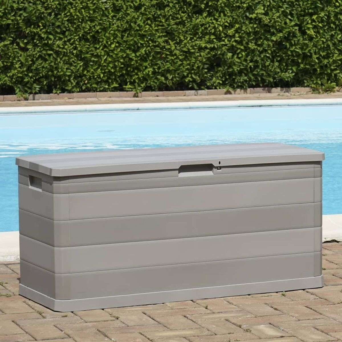 Graue Aufbewahrungsbox mit Deckel. Der Hintergrund ist ein Pool und grüne Büsche.