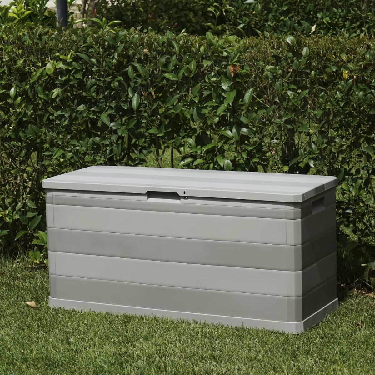 Graue Outdoor-Aufbewahrungsbox aus Kunststoff in einem grasbewachsenen Bereich mit Hecke.