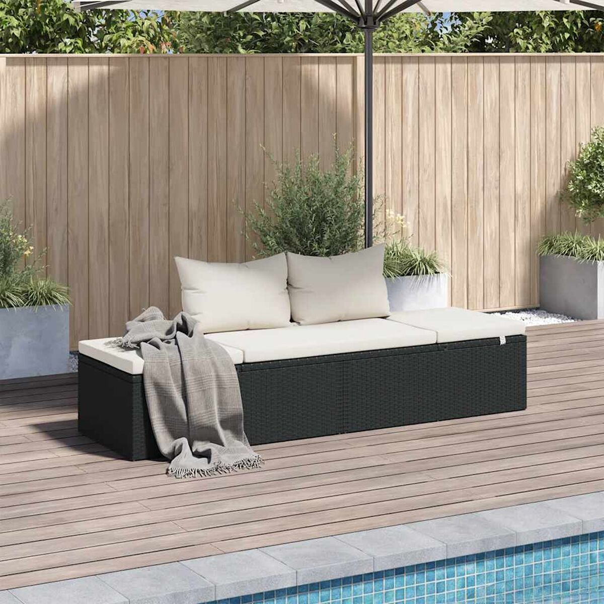 Schwarze Korbbank mit weißen Kissen und grauer Decke. Holzterrasse und Pool. Sonniger Tag.