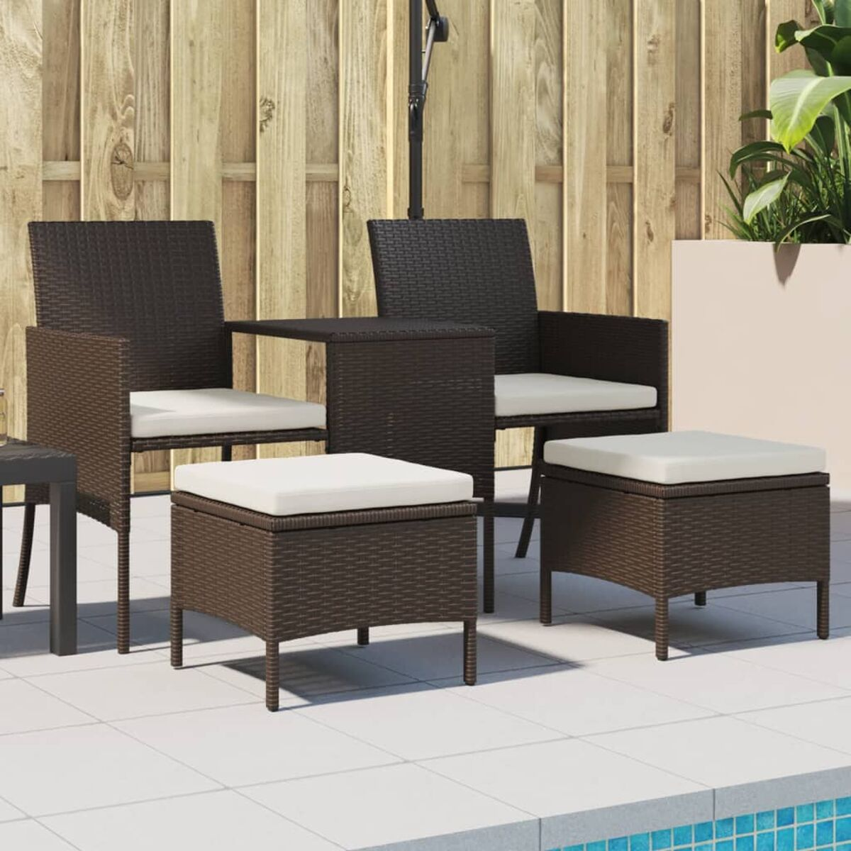 Ein Terrassenset mit zwei Stühlen und zwei Ottomanen mit weißen Kissen und einem kleinen Tisch. Braunes Korbgeflecht.