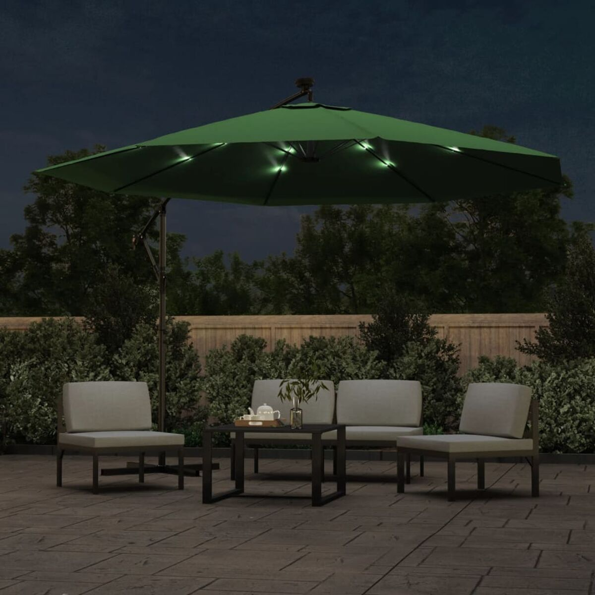 Outdoor-Sitzbereich bei Nacht mit grünem Schirm. Lichter sind an, es gibt Stühle und einen Tisch.