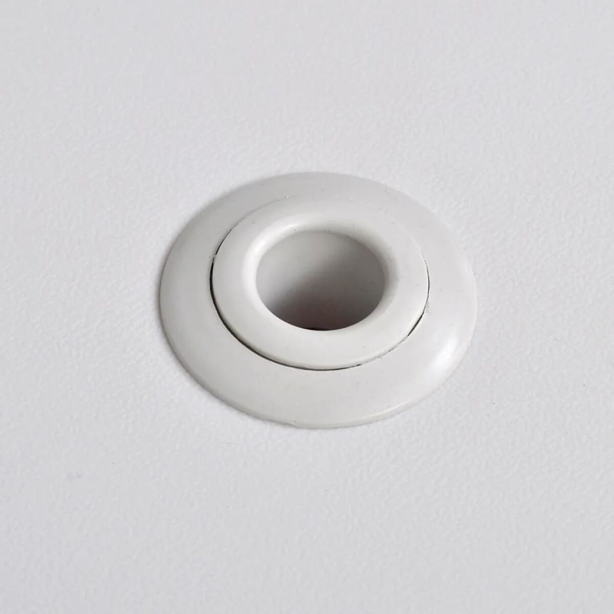 Eine weiße Vorrichtung auf einer weißen Oberfläche. Sie hat ein zentrales Loch, das von einem Ring umgeben ist.