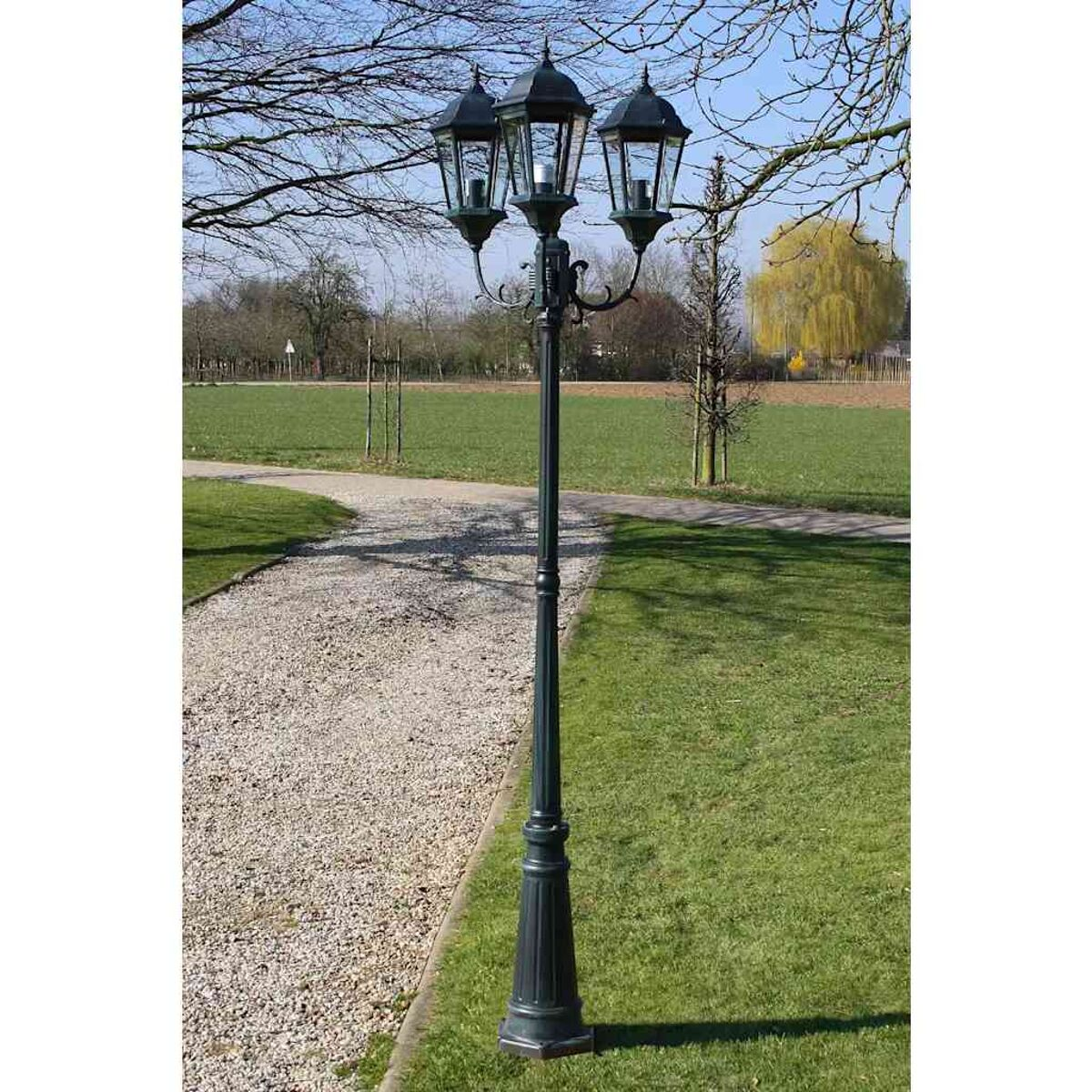 Eine dunkelgrüne Straßenlaterne. Drei Lampenköpfe befinden sich auf einer hohen Stange.