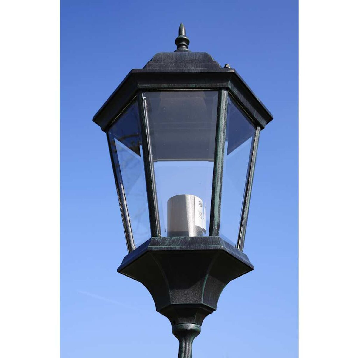 Eine schwarze und bronzefarbene Außenlampe mit klarer Glasabdeckung vor blauem Himmel.