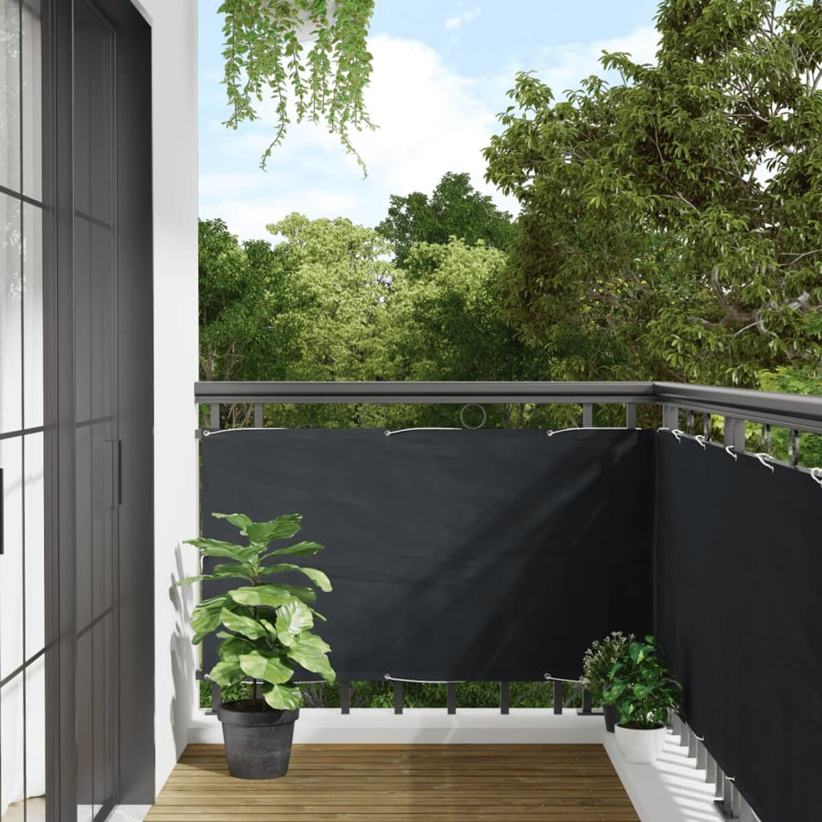 Balkon mit schwarzem Geländer, schwarzem Sichtschutz, Holzboden und Pflanzen. Grüne Bäume im Hintergrund.
